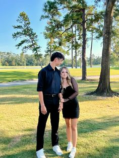 a man and woman standing next to each other in front of some trees on the grass