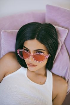 a woman laying on top of a bed wearing pink sunglasses and a white tank top