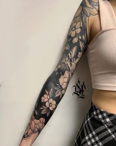 a woman's arm with flowers and leaves on it, next to a white wall