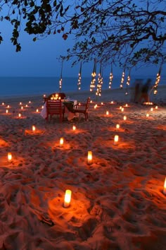 many lit candles are on the sand near chairs and tables at an outdoor dining area