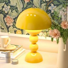 a yellow lamp sitting on top of a table next to a vase filled with flowers