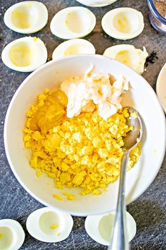 a bowl filled with eggs and yogurt on top of a table next to spoons