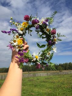 a person holding up a wreath made out of flowers in the middle of a field