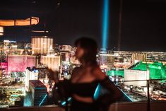 a woman standing on top of a tall building next to a cityscape at night