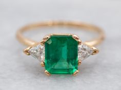 Pretty and luxurious, this emerald and diamond ring has a timeless design. The emerald is a vibrant Kelly green with excellent clarity. The trillion-cut diamonds don't overwhelm the center stone and instead enhance it with just the right amount of sparkle. Highly versatile, this ring is a true classic!Metal: 14K Yellow GoldGem: Emerald 1.41 CaratsGem Measurements: 7.3 x 6.2 mm, Emerald CutAccents: 2 Diamonds totaling .33 Carats, SI in Clarity, H in ColorRing Size: 6.75Marks: “14K*” Stamped on th