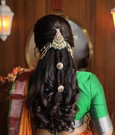 a woman with long hair wearing a green and orange saree, standing in front of a mirror