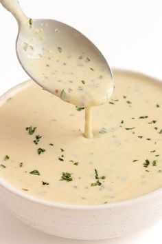 a white bowl filled with broccoli soup and a ladle full of dressing