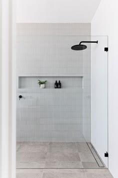 a white tiled bathroom with black and white accessories on the shower head, along with two planters