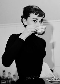 a woman drinking from a cup while holding a plate