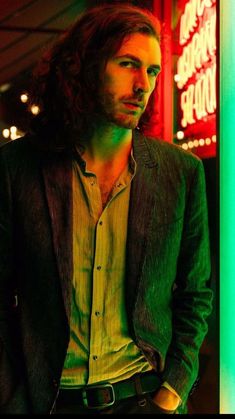 a man with long hair standing in front of neon signs and looking at the camera