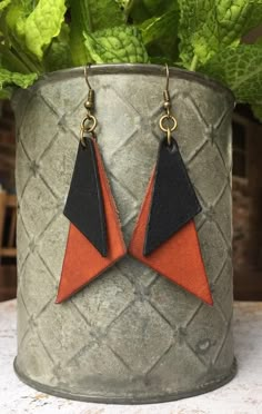 an orange and black triangle shaped leather earrings on a potted plant with green leaves in the background