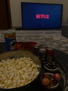 a bowl of popcorn and cans of soda on a table in front of a television