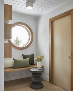 a round window in a white room with wood flooring and pillows on the bench