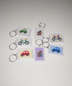 six cross stitch keychains with cars and bicycles on them, all in different colors