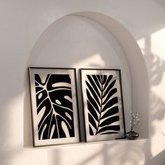 two black and white paintings on a wall next to a vase with flowers in it