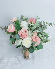 a bridal bouquet with pink and white flowers on a lace tablecloth against a white wall