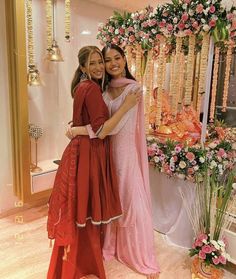 two young women hugging each other in front of a floral display at a wedding reception