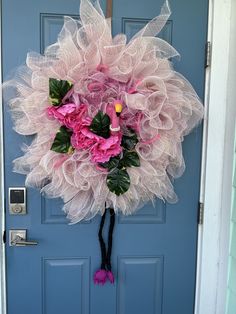 a pink and white wreath hanging on the front door to a blue door with flowers in it