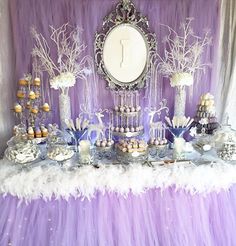 a table topped with lots of desserts next to a purple wall covered in frosting