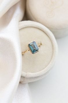 an engagement ring with a blue topaz sits in a white velvet box on the floor