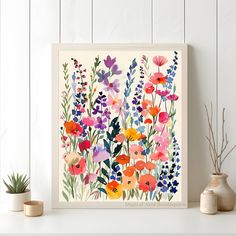 an art print of colorful flowers on a white shelf next to two potted plants