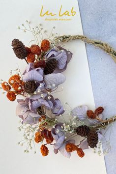 a wreath made out of dried flowers and pine cones on top of a piece of paper