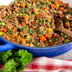 a blue bowl filled with ground beef and veggies next to a wooden spoon