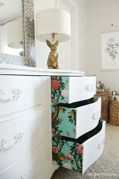 a white dresser topped with drawers and a lamp next to a wall mounted mirror in a bedroom