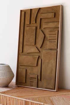 a vase sitting on top of a wooden shelf next to a wall mounted art piece