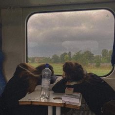 two people sitting at a table with their backs to each other looking out the window