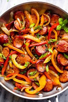 a pan filled with sausages and peppers on top of a marble countertop next to a fork