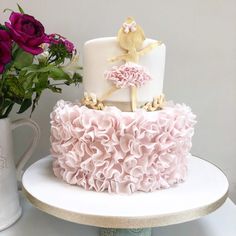 a white cake with pink ruffles sitting on top of a table next to flowers