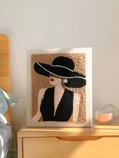 a woman wearing a black hat on top of a wooden dresser next to a white wall