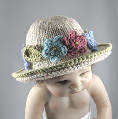 Hand-knit of soft cream-colored cotton yarn with a wide brim to protect little eyes from the sun, this adorable hat is perfect  as an Easter bonnet, for the summer or any time. A garland of flowers encircles the hat, picking up the colored flecks in the yarn, and adding sophisticated style. The palette offers two versions, one with pastel flowers and one with brighter flowers, all in the same tones. The hat comes in 3 sizes, and because it is knit and quite stretchy you may find that it fits lon Cute Beige Wide Brim Hat, Playful Adjustable Cream Hat, Adjustable Knitted Cream Bonnet, Adjustable Cream Knitted Bonnet, Cream Handmade Sun Hat With Curved Brim, Cute Adjustable Yarn Mini Hats, Handmade Cream Sun Hat With Curved Brim, Cream Sun Hat With Handmade Curved Brim, Cute Knitted Hat For The Beach