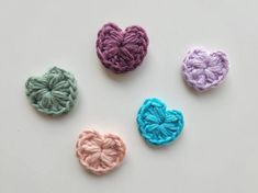 four crocheted hearts arranged in different colors on a white surface with one heart shaped at the center