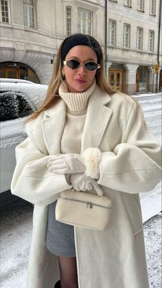 a woman is standing outside in the snow with her hand on her hip and wearing a white coat