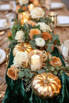 a long table with candles, flowers and pumpkins on the centerpiece is decorated with greenery