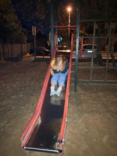 a young child is sliding down a slide at night time in the playground with no one on it