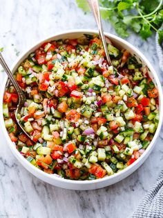 a white bowl filled with cucumber salad and two silver spoons on the side