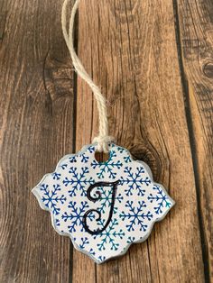 a ceramic ornament with the letter f on it hanging from a rope against a wooden background