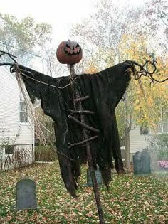 a scarecrow with a pumpkin on his head hanging from a tree in a yard