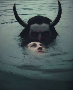 a woman with horns swimming in the water next to a man's head and nose