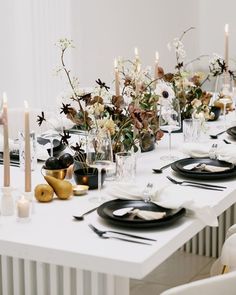 the table is set with black and white plates, silverware, candles and flowers