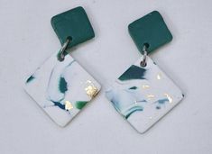 two square white and green earrings with gold flecks on the sides, hanging from metal hooks