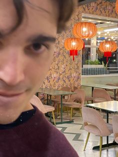 a man is looking at the camera in a restaurant with lanterns hanging from the ceiling