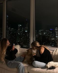 two women sitting on a couch with a dog in their lap looking out the window