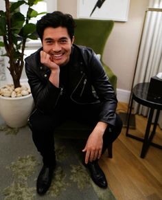 a man sitting on the floor in front of a potted plant and smiling at the camera