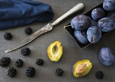 some blackberries and plums are next to a knife