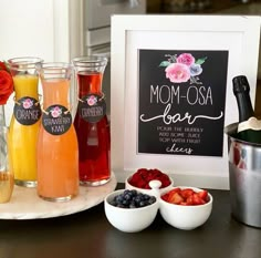 a table topped with drinks and fruit next to a chalkboard that says mom - osa bar