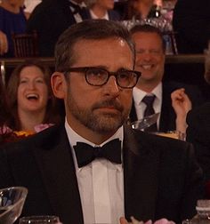 a man in a tuxedo sitting at a table with other people and laughing